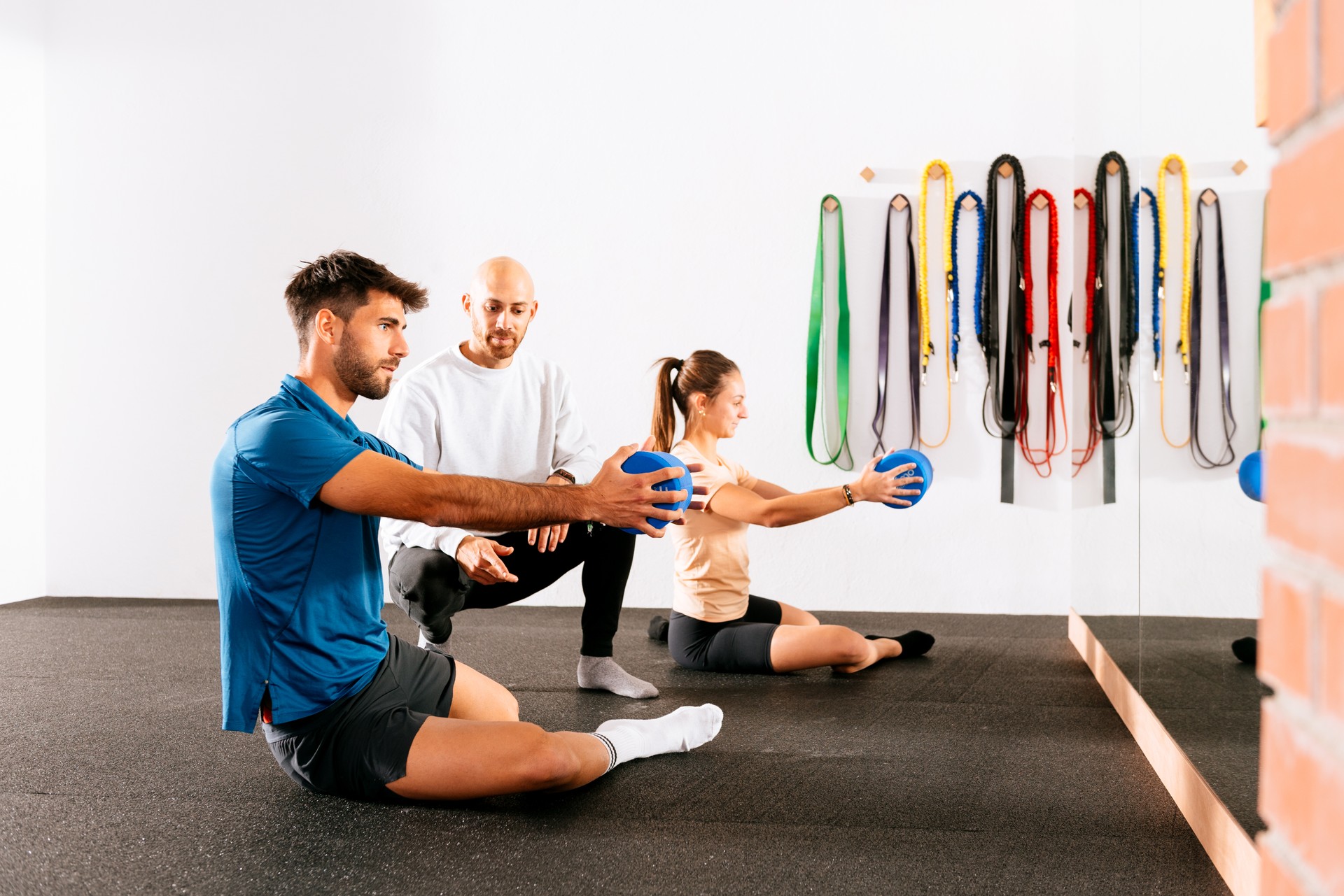 Young male and female with instructor doing stretch exercise with elastic roller